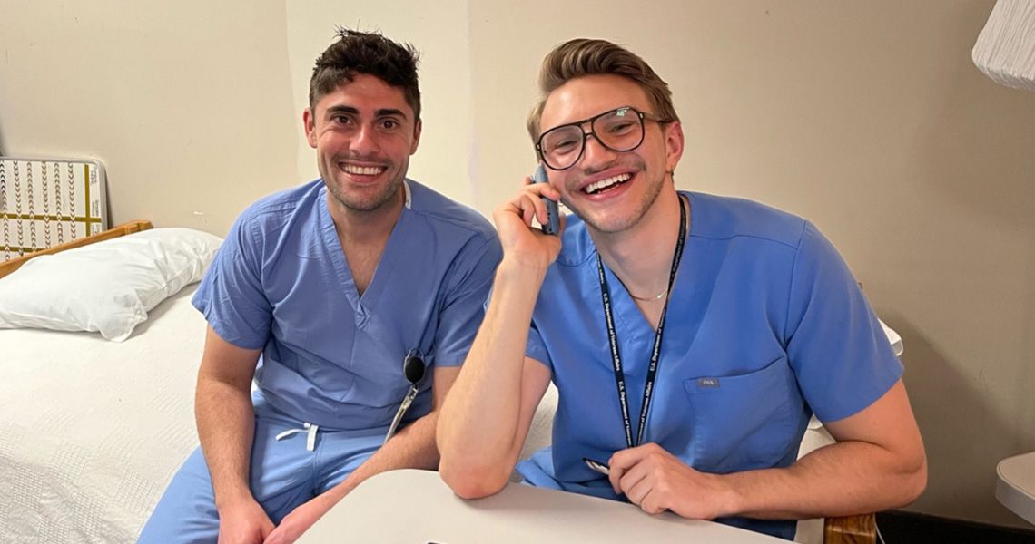 two medical professionals smiling and seated on a medical bed